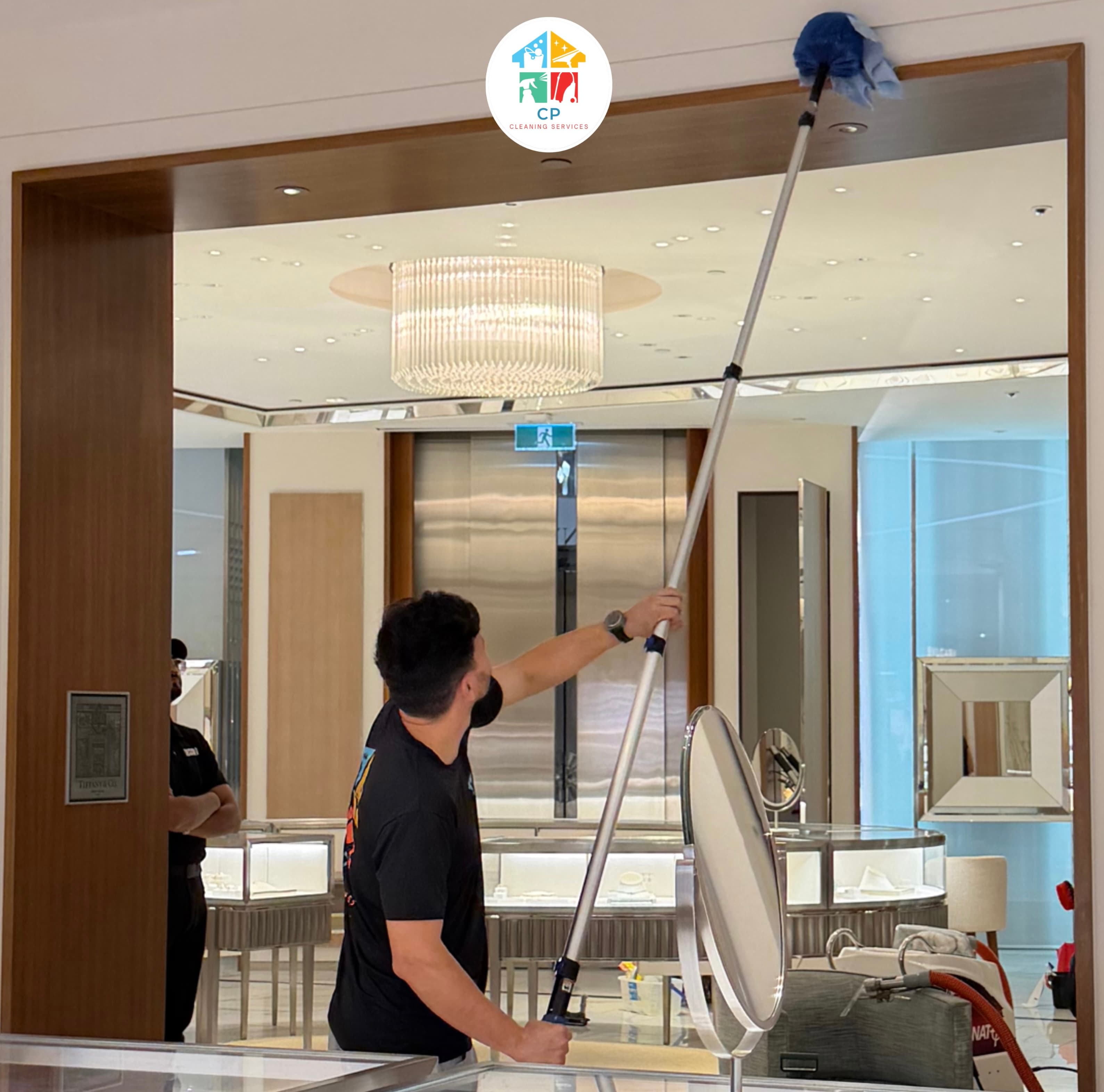 Professional cleaner using a long extension pole to dust high surfaces in a luxury store.