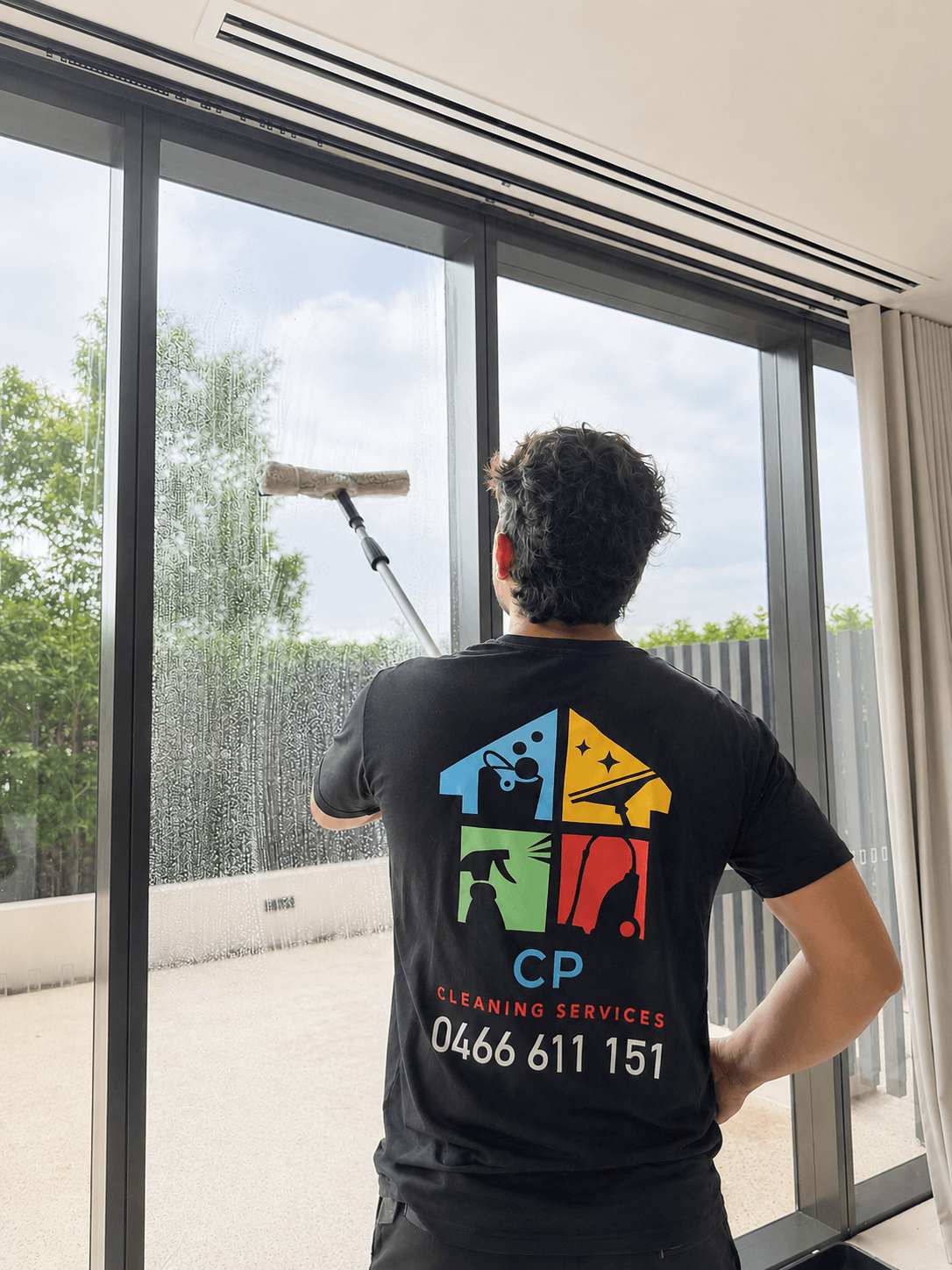 Professional cleaner in a branded shirt uses a squeegee to wash a large glass window.